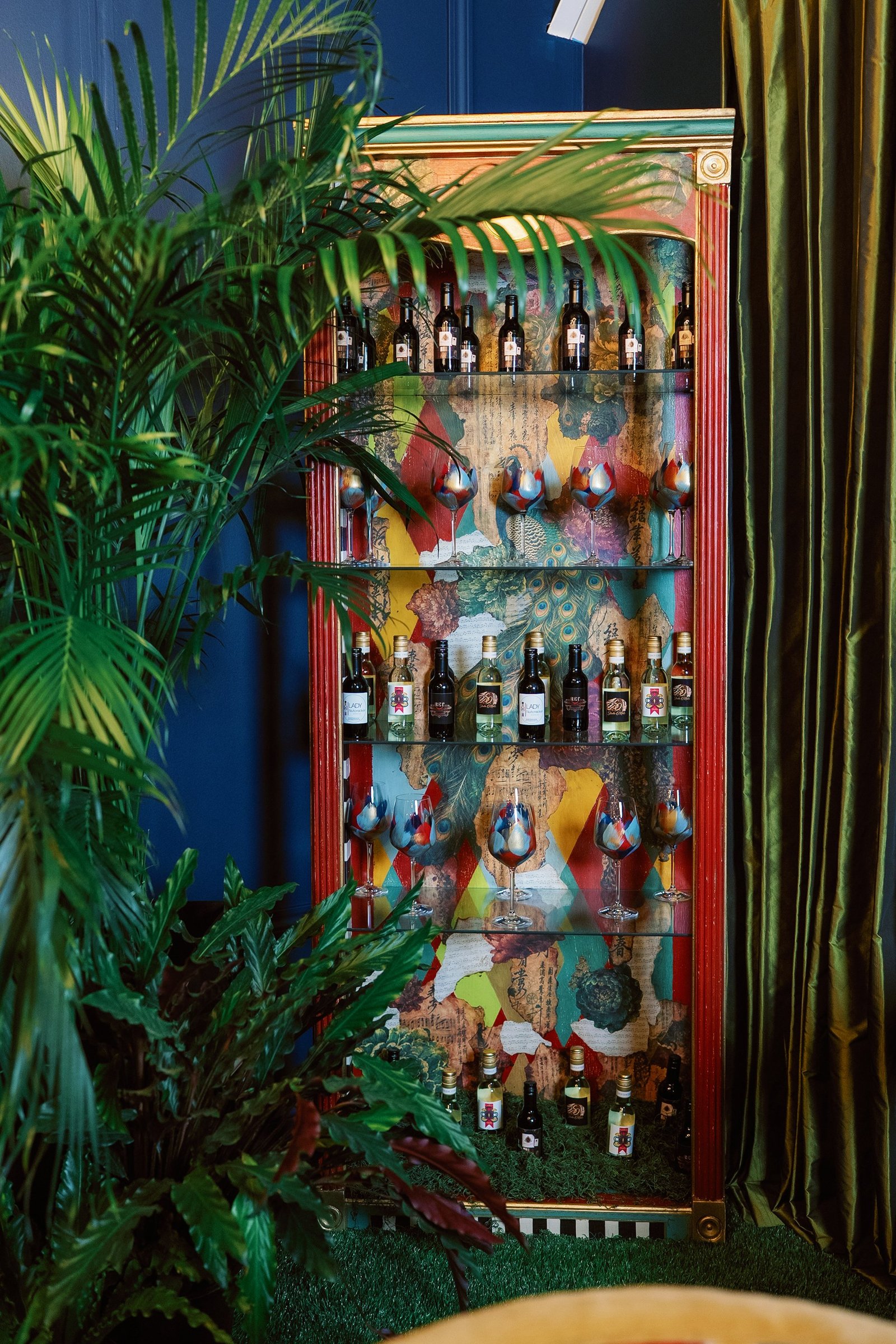 Full view of the red-framed peacock display cabinet stocked with wine and glassware
