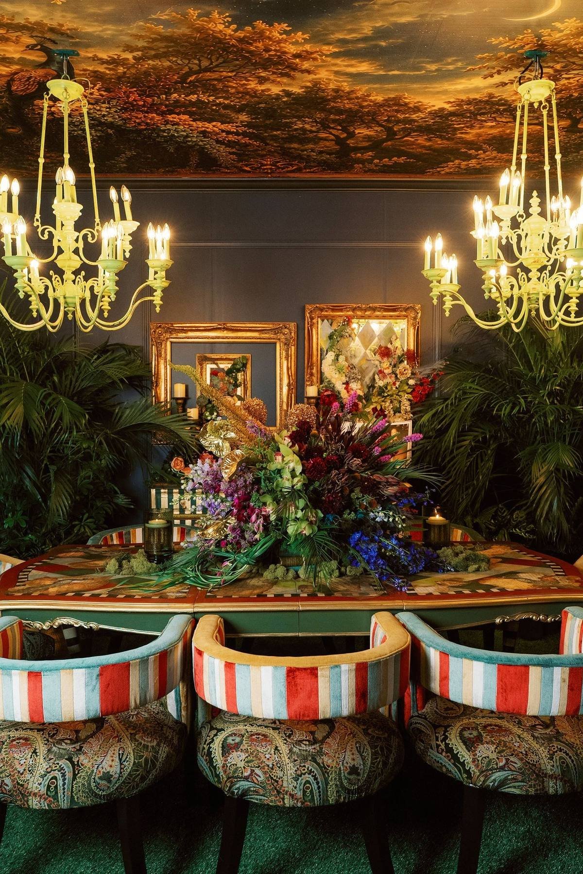 Maximalist dining room with hand-painted ceiling mural, lime-green chandeliers, green grass carpet, and ornate peacock-themed decor