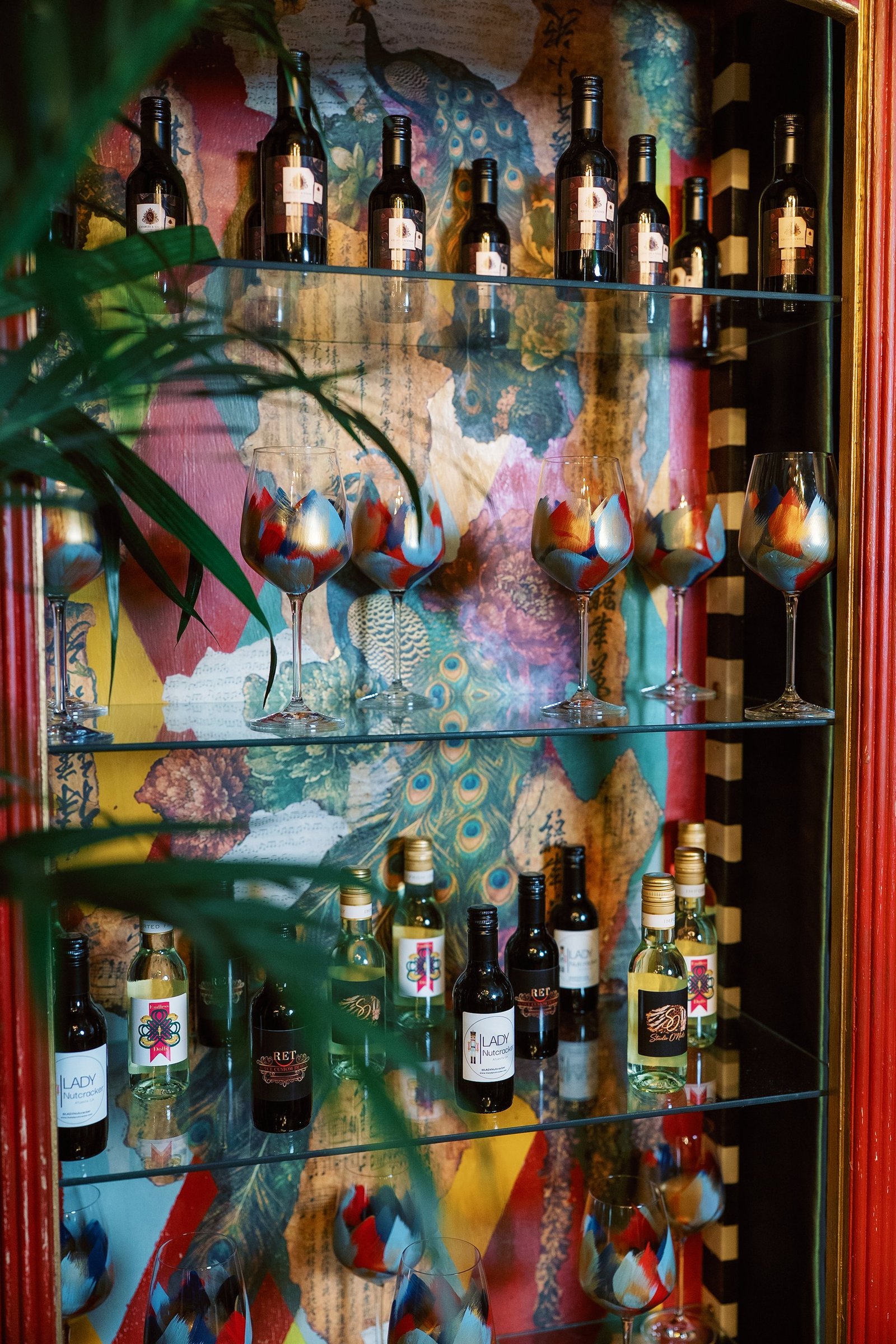 Interior shelves of the display cabinet with hand-painted wine glasses and colorful peacock-motif wallpaper