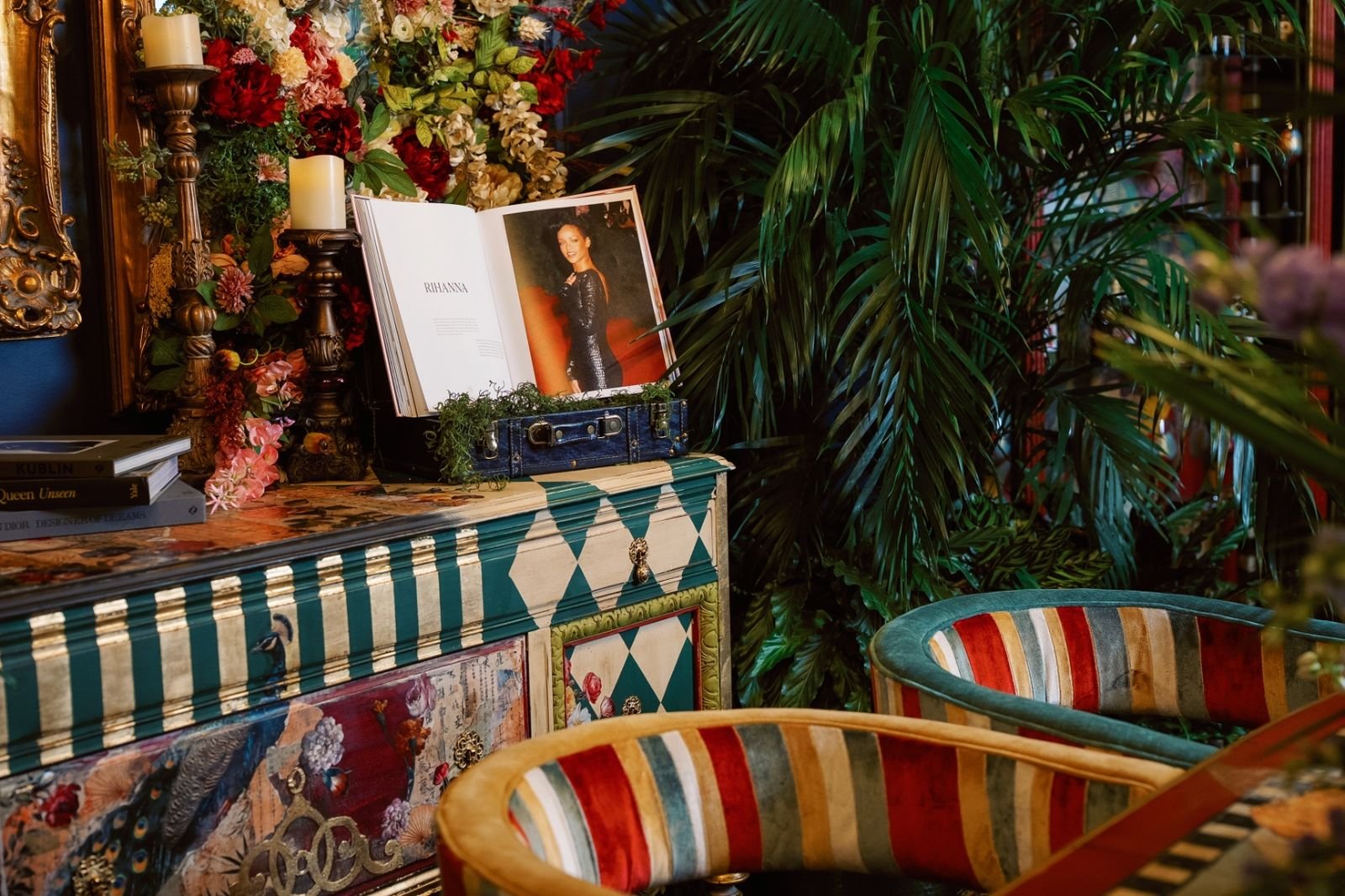 Styled vignette on the sideboard top with stack of books, candles in brass holders, and a dense floral arrangement